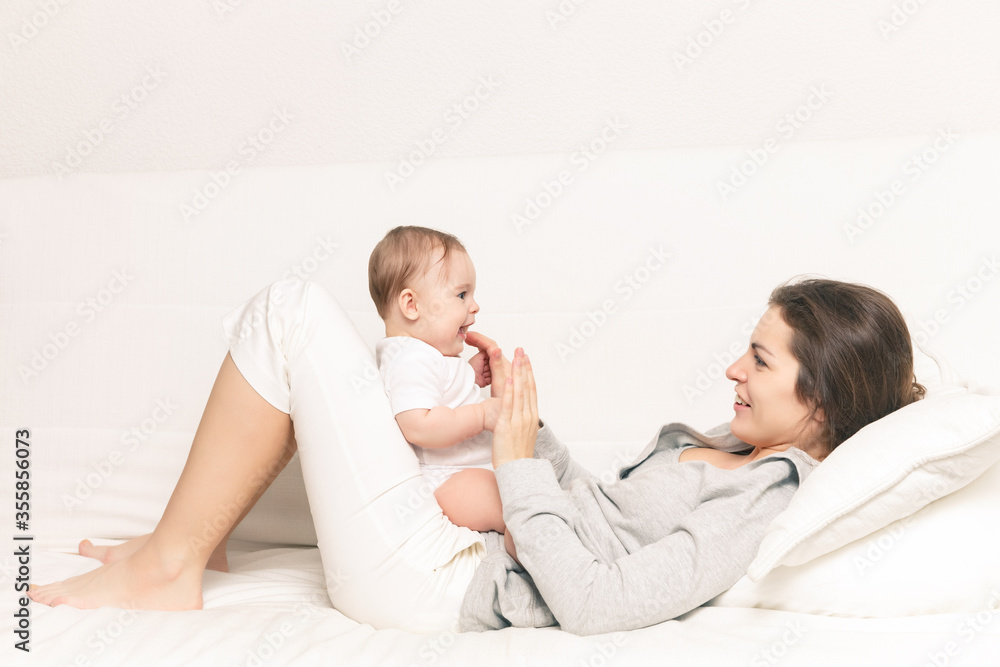 Happy mother playing with baby on white sofa