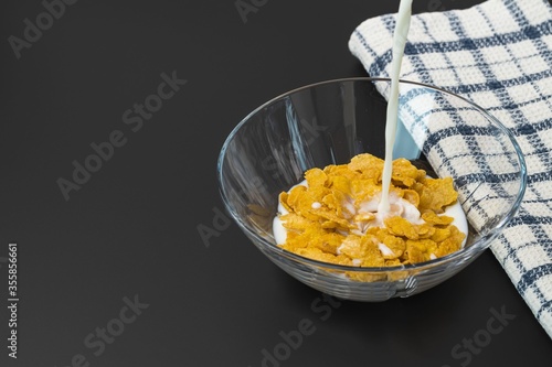 View of process of pouring milk into glass bowl with cornflakes. Healthy eating concept. Healthy food background.