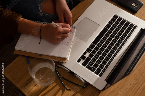 home work space - work from home concept - girl writing notes with a laptop sitting on a sofa by a wooden desk