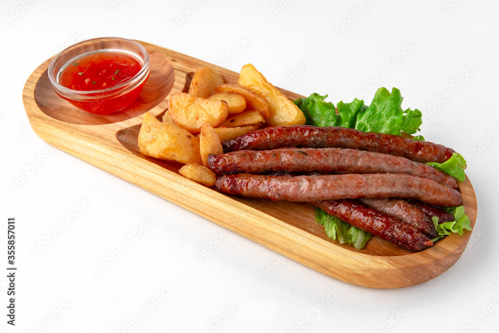 Hunting sausages with sauce and potatoes on a wooden stand. Banquet festive dishes. Gourmet restaurant menu. White background. Hunting sausages with sauce and potatoes on a wooden stand. Banquet festive dishes. Gourmet restaurant menu. White background.