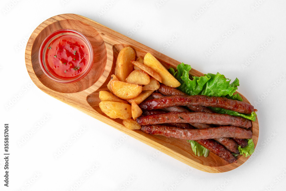Hunting sausages with sauce and potatoes on a wooden stand. Banquet festive dishes. Gourmet restaurant menu. White background. Hunting sausages with sauce and potatoes on a wooden stand. Banquet festive dishes. Gourmet restaurant menu. White background.