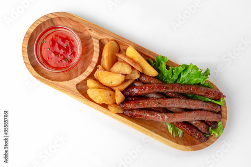 Hunting sausages with sauce and potatoes on a wooden stand. Banquet festive dishes. Gourmet restaurant menu. White background.
