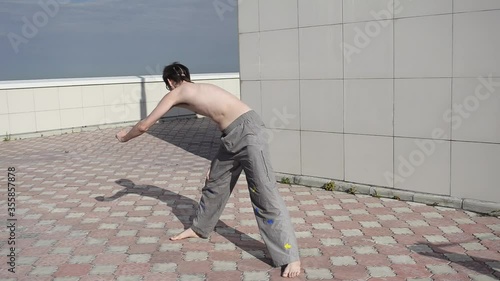 A man plays sports on the roof. A complex set of exercises based on gymnastics and karate.