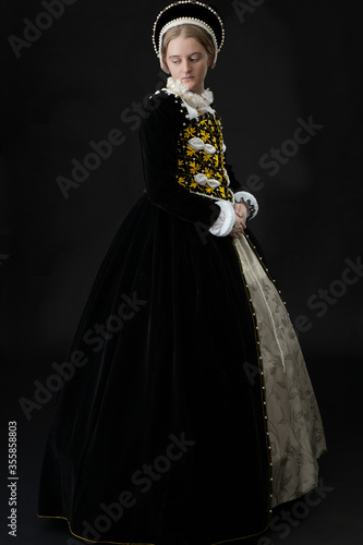 Photography A young woman in black velvet Elizabethan costume standing against a dark studio
