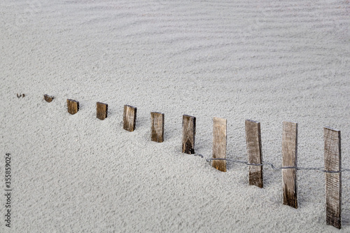 storm fence disappears into drifting beach sand dune