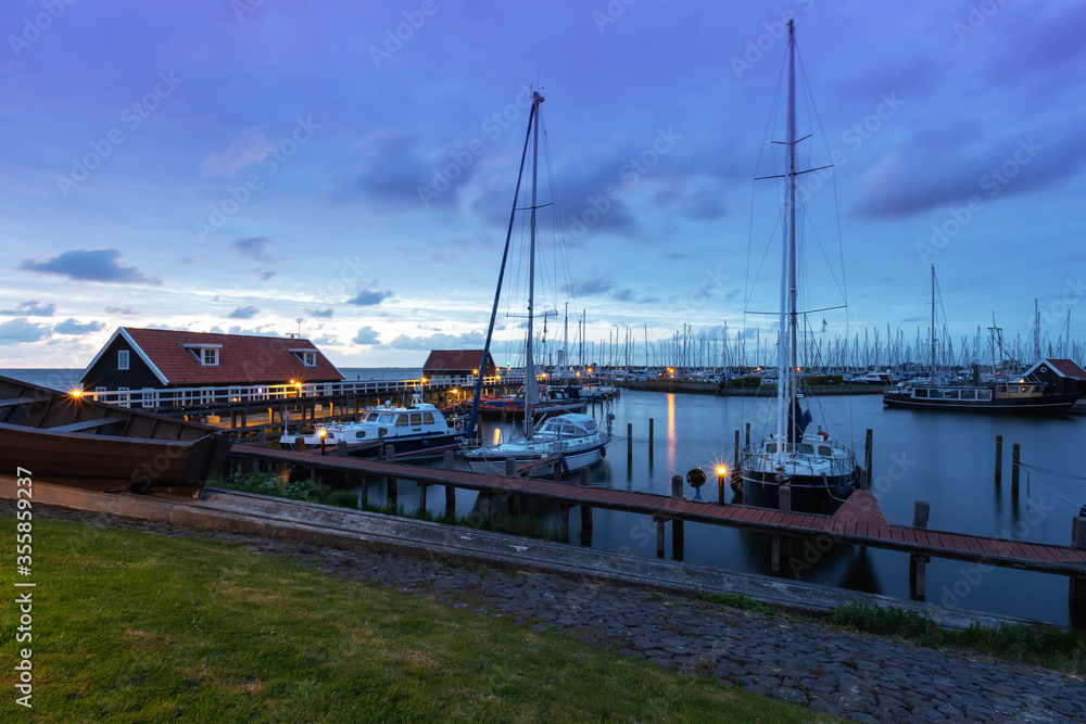 the Netherlands - Hindeloopen - a magical view of the evening harbor lit by lamps and the stone path leading to a wooden pier where sailboats and boats are moored.