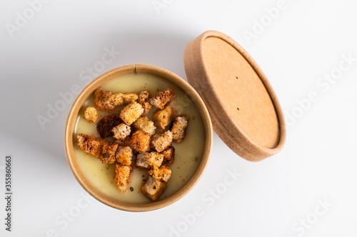 Potato cream soup with croutons in craft containers on a white background. Vegetable soup to go, food delivery