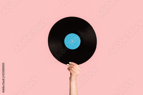 Girl hand showing retro vinyl gramophone record on pink background, closeup photo