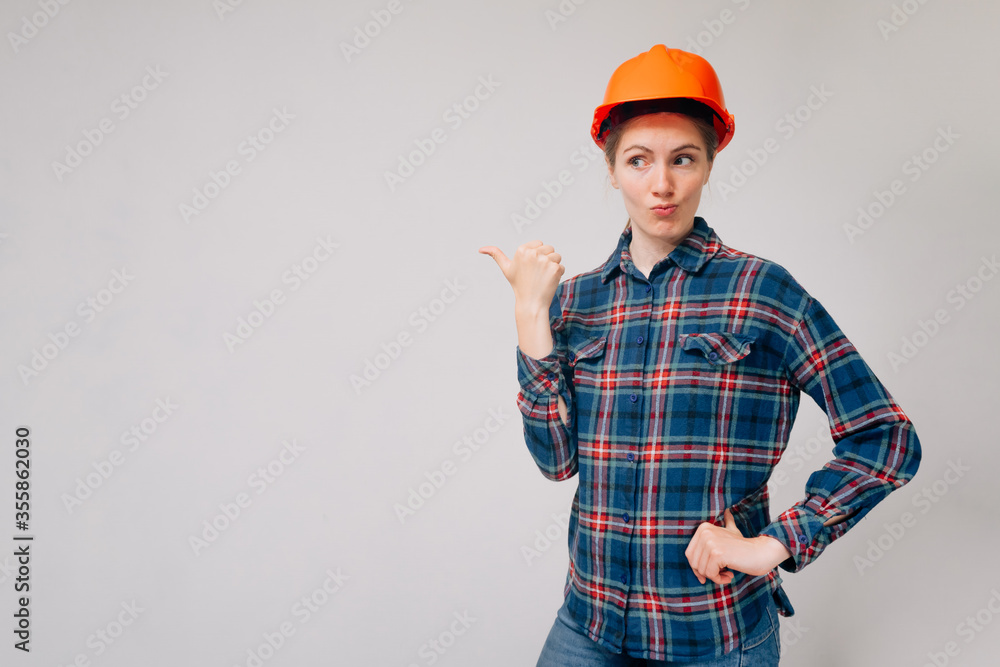 Portrait of an indignant builder's girl pointing her finger to the side against a light background. Portrait of an indignant builder's girl pointing her finger to the side against a light background.