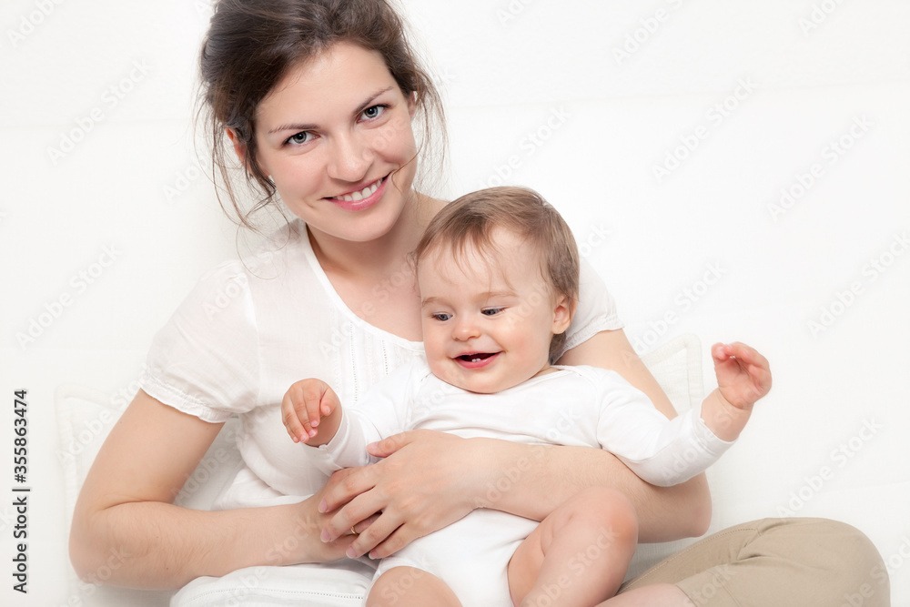 Happy mother playing with baby on white sofa Happy mother playing with baby on white sofa