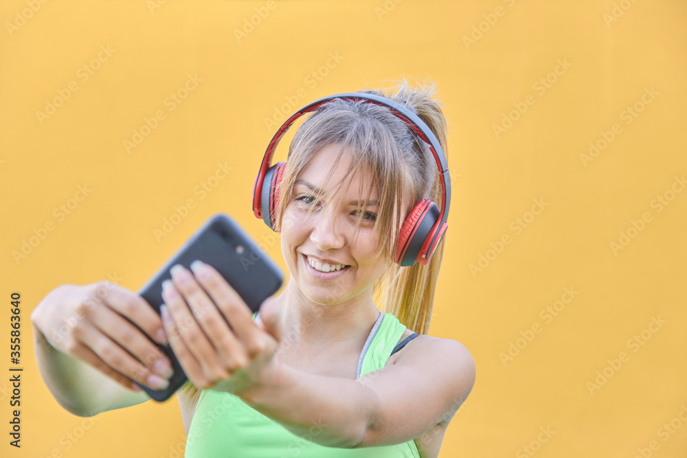 Naklejka premium The pretty girl who listens to smatphone music makes a selfie