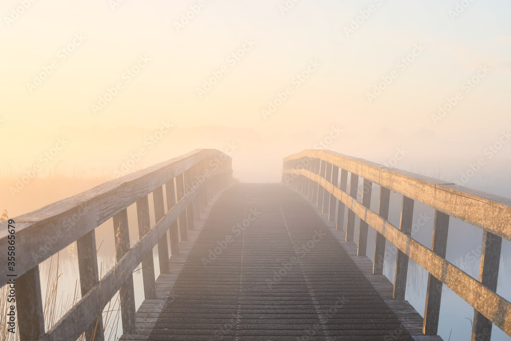Obraz premium wooden bridge in dense fog at sunrise