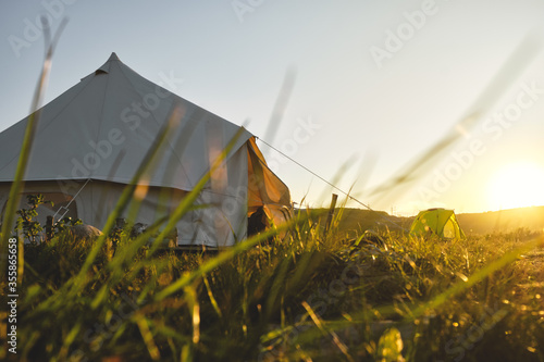 path to a glamping tent in the middle of a green field in the sunset rays. Camping and outdoor concept.