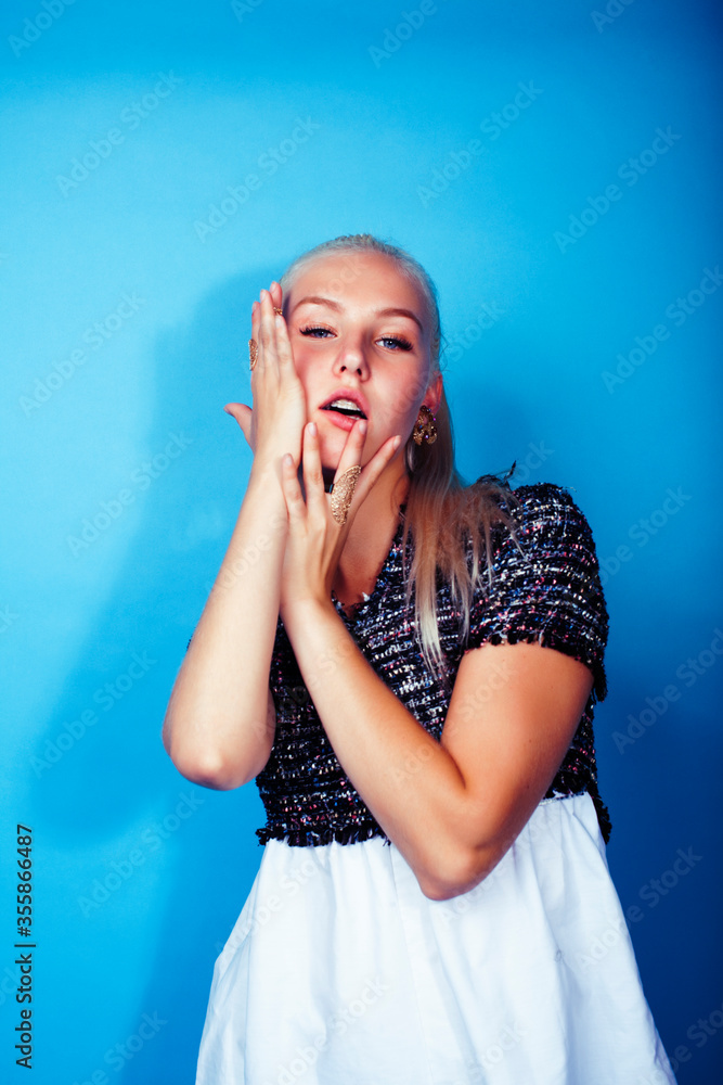 young pretty teenage modern hipster girl posing emotional happy on blue background, lifestyle people concept