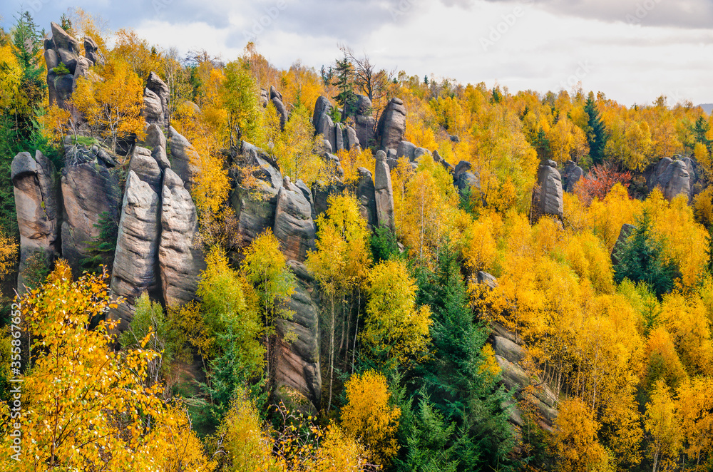 Fototapeta premium Tall rock formations pointing out of the colorful autumn forest, Czech Republic