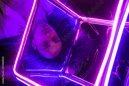 Portrait of the Young Handsome emotional man in an unbuttoned white shirt with neon coub. Neon Room. Old 90's retro style. Reflect of neon words near male. Selective focus. photo