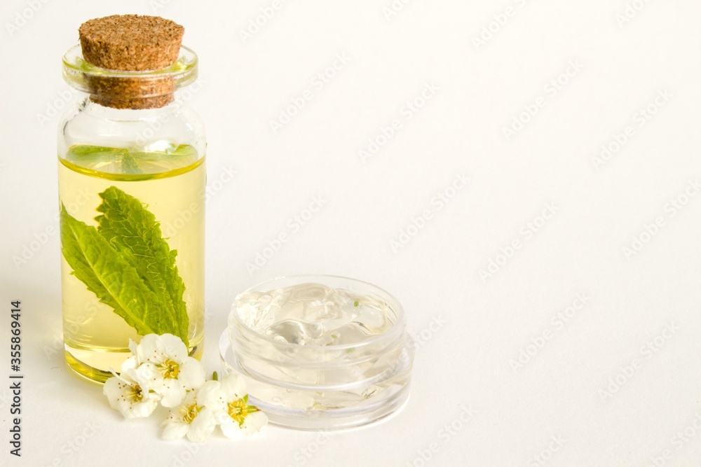 Beautiful photo of small bottle with cork stopper filled with fantastic fragrant oil, essential oils and peppermint and gallipot with aloe vera gel with flowers Beautiful photo of small bottle with cork stopper filled with fantastic fragrant oil, essential oils and peppermint and gallipot with aloe vera gel with flowers