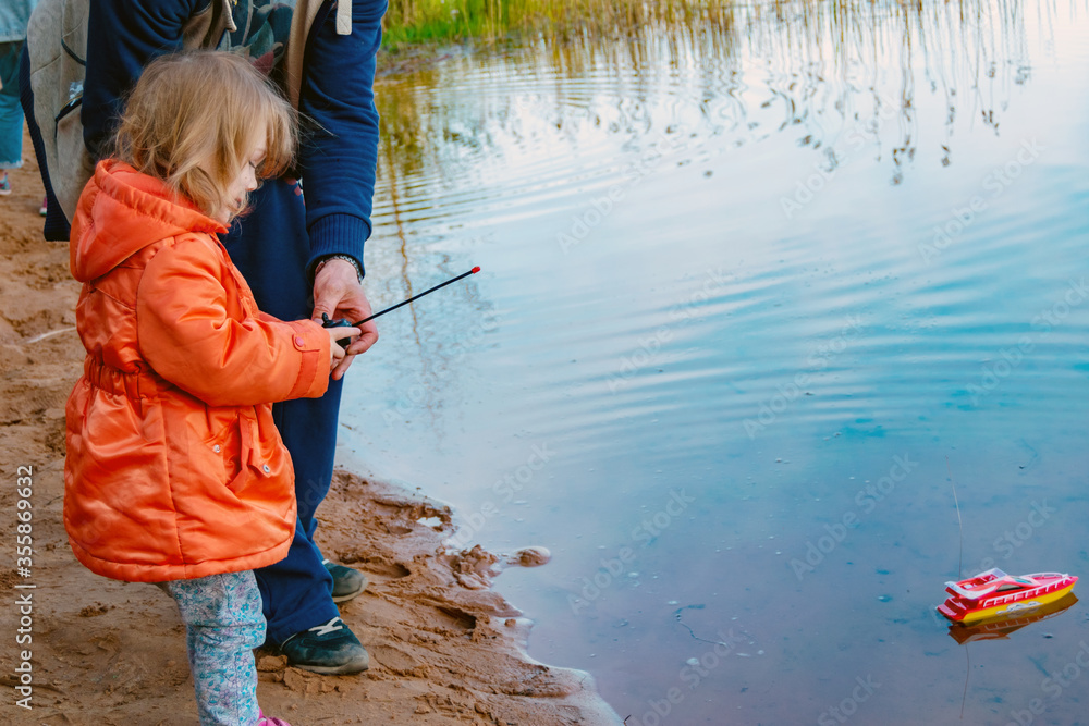 The girl on the sandy shore of the lake in her hands is a remote control from a toy boat. The girl on the sandy shore of the lake in her hands is a remote control from a toy boat.