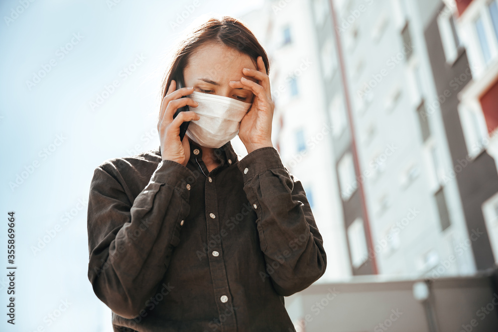 Girl in a medical mask talking on a cell phone on the street. Reported bad news