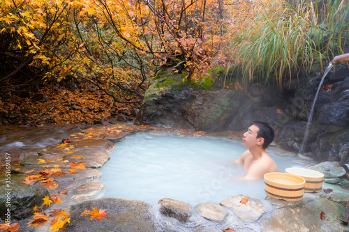 Young man soak in outdoor onsen hot spring in autumn  photo