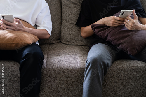 man is using a smartphone for the internet while relaxed sitting on the sofa at his modern home. young people are texting on mobile devices while on the couch. a guy is holding the telephone.