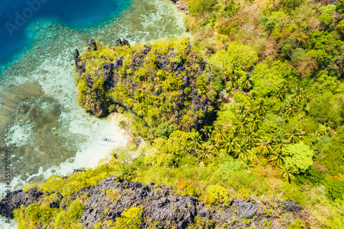 Aerial drone view of secluded beach in jungle with tropical coral reef and small sandy beach surrounded by huge cliffs