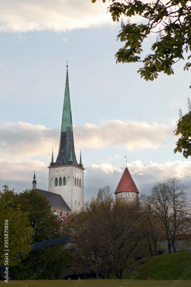 Fototapeta premium Tower of the city wall and Oleviste Catholic Church at the Old city of Tallinn in Estonia at the early spring time. Gothic Scandinavian architecture of medieval charming city of Tallinn Old Town.