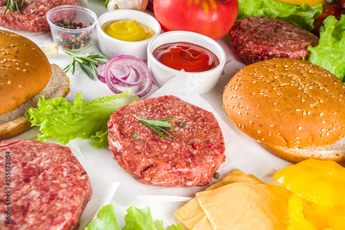 Cooking burger background. Set various cheeseburger  and beefburger ingredients - bun, tomatoes, onion, lettuce, sauces, cheese and raw burger cutlets, ready for barbecue grill. Burger bbq party fest 