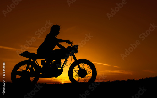 Black silhouette of a girl on a retro custom bike. Motorcycle and girl on a background of sunset over the evening.