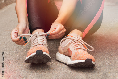 Fototapeta Naklejka Na Ścianę i Meble -  Running shoes runner woman tying laces preparing for workout. Jogging girl exercise motivation heatlh and fitness. Female runner. Get laced up and get going. Motivation and overcoming concept.
