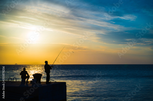 Silhouette of people fishing by the sea with twilight blue hours sky