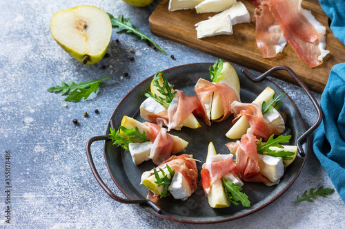 Summer snacks. Pear appetizer with jamon, arugula and brie cheese on a light stone table. Copy space.