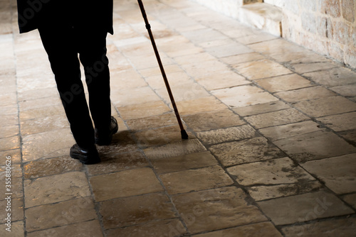 Old man legs walking with walking stick on stone tiles