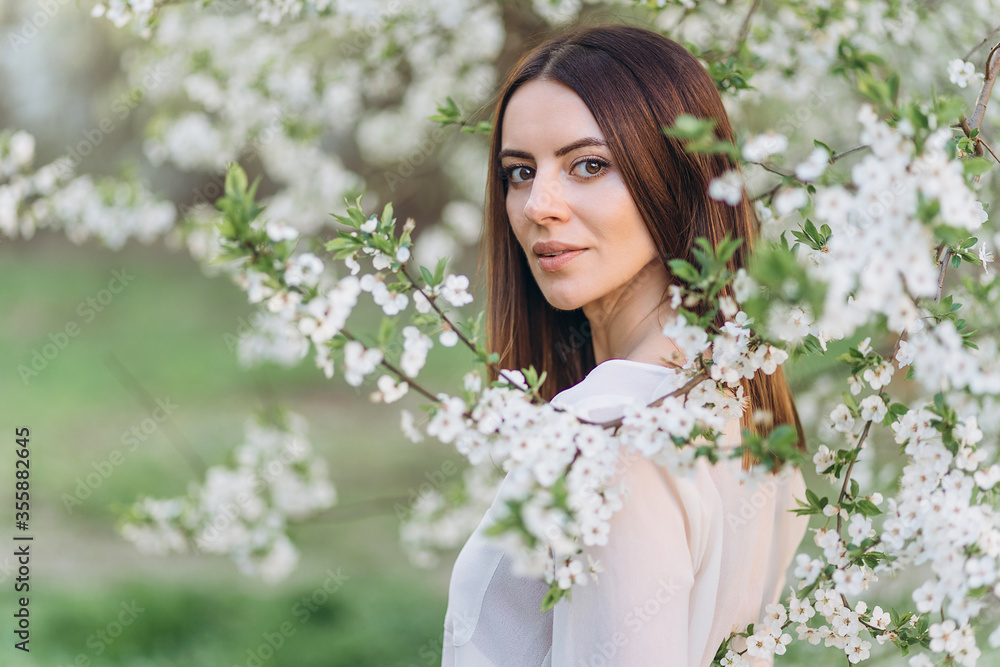 Amazing young woman posing in Blooming tree orchard at spring. Beautiful happy young woman enjoying smell in a flowering spring garden