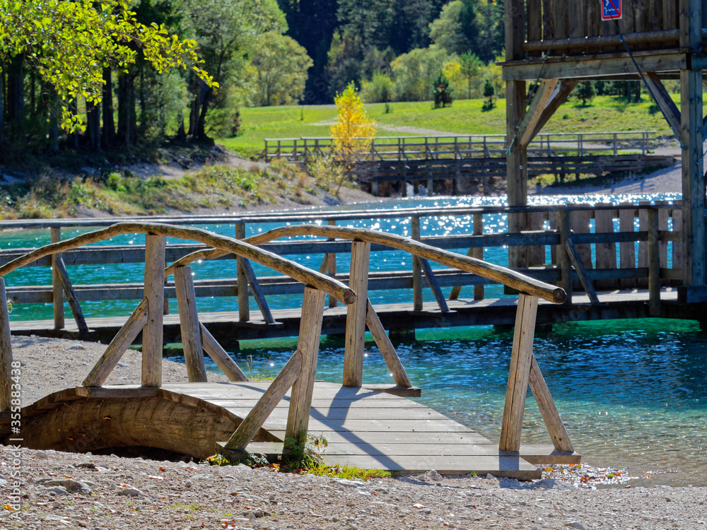 Wooden bridge on hiking path around the cristal clear artificial alpine lake Jasna with view tower that is used as jump platform to jump into a lake in background. It is must see location in Slovenia. Wooden bridge on hiking path around the cristal clear artificial alpine lake Jasna with view tower that is used as jump platform to jump into a lake in background. It is must see location in Slovenia.