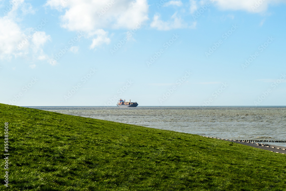 Scenery at the seaside with large container ship passing the dyke at Breskens, Netherlands
