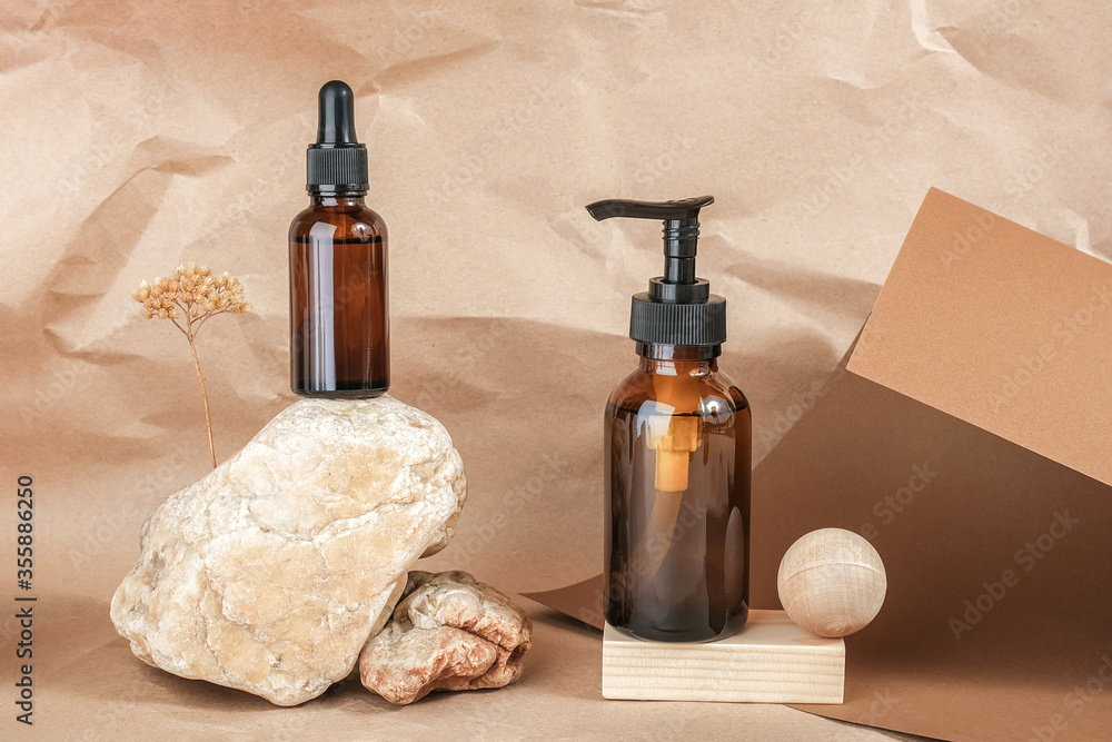 Naklejka premium Brown glass bottles of cosmetic products on stone and wooden geometric shapes on beige craft paper background. Natural Organic Spa Cosmetic Beauty concept Front view Mockup