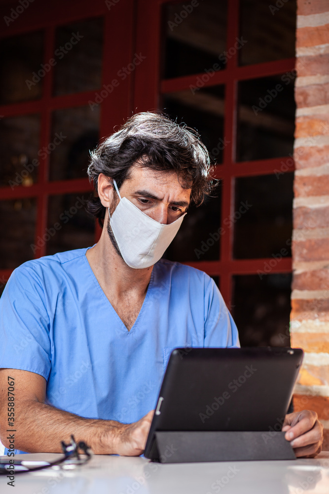 Doctor with face mask working with his tablet in the garden of his house. Doctor with face mask working with his tablet in the garden of his house.