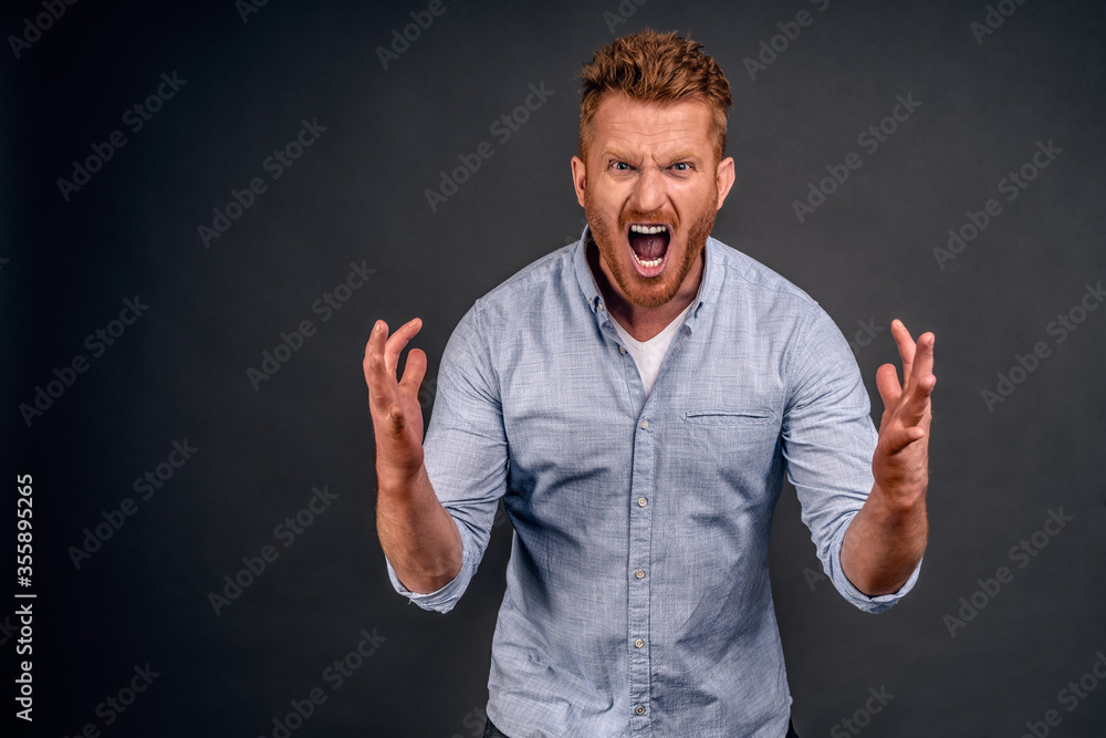 Guy being cheated on, feeling mad and angry, shouting at guilty wife, shaking palms in anger and yelling while bending towards camera, being pissed off and filled with hate over gray background Guy being cheated on, feeling mad and angry, shouting at guilty wife, shaking palms in anger and yelling while bending towards camera, being pissed off and filled with hate over gray background