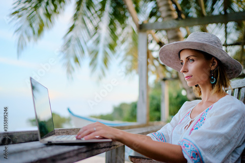 Technology and travel. Working outdoors. Freelance concept. Pretty young woman using laptop in cafe on tropical beach.