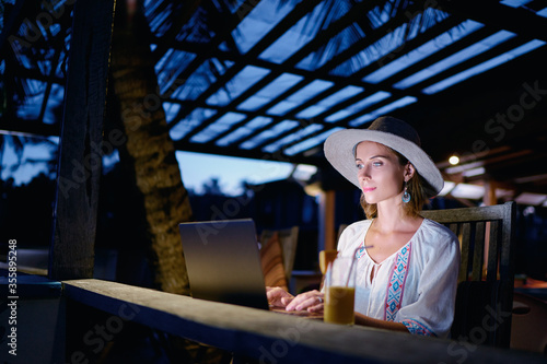 Work and travel. Study and vacation. Working outdoors. Freelance concept. Pretty young woman using laptop in tropical beach bar cafe. © luengo_ua