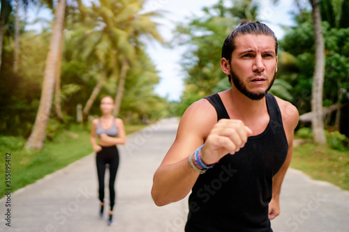 Healthy lifestyle. Jogging outdoors. Young man and woman is running under palm trees.