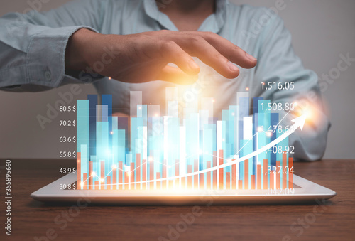 Businessman holding tablet with virtual statistic hologram graph and chart. Stock investor have to analysis profit and business data before investment.