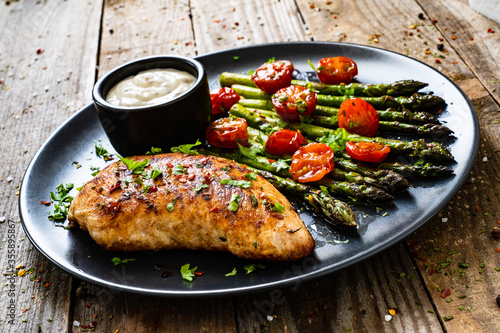 Tasty roast chicken breast, green asparagus, cherry tomatoes and garlic dip on wooden table 