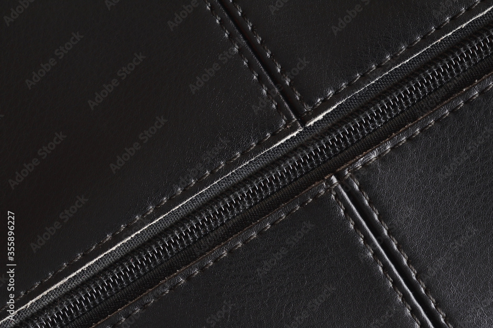 Black leather background with seams and a plastic zipper. Leather bag element. Closeup