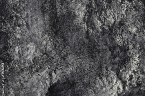 Texture of natural sheepskin. Worn uneven gray fur background. Bumpy surface of a used lambskin material. Top view. Closeup