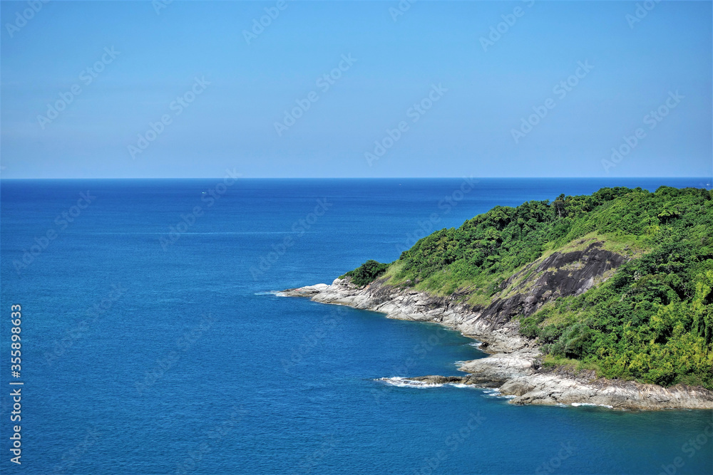 Tropical island in the sea. A small island with gently sloping rocky shores and vibrant tropical vegetation amid calm aquamarine water. Clear blue sky.