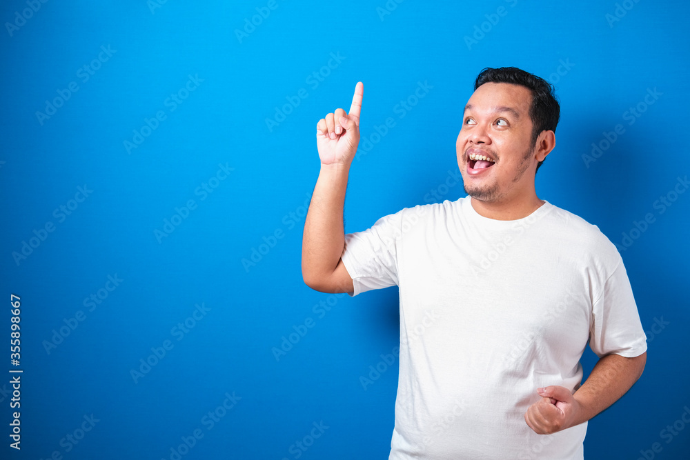 Photo image of Fat Asian man in white t-shirt looked happy thinking and looking up, having good idea. Half body portrait against blue background with copy space Photo image of Fat Asian man in white t-shirt looked happy thinking and looking up, having good idea. Half body portrait against blue background with copy space