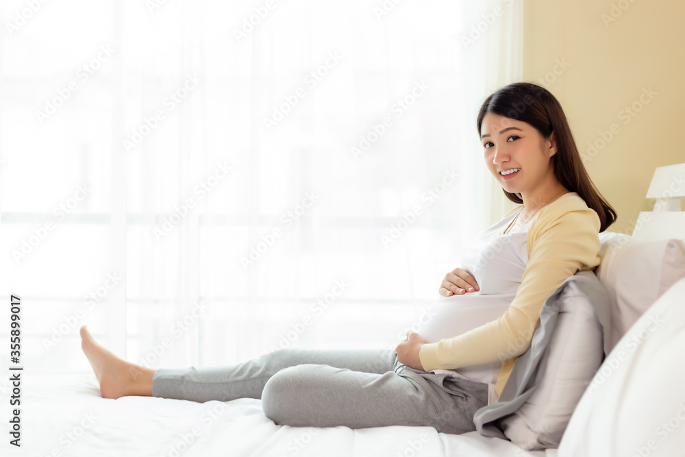 Happy pregnant young asian woman touching belly, love her baby or fetus with happiness smile face, look at camera. Pregnancy girl waiting and expecting baby has good health pregnancy, mother concept Happy pregnant young asian woman touching belly, love her baby or fetus with happiness smile face, look at camera. Pregnancy girl waiting and expecting baby has good health pregnancy, mother concept
