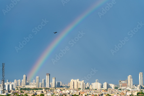 Aerial cityscape shot of buildings in gurgaon delhi noida with a rainbow behind them on a monsoon day